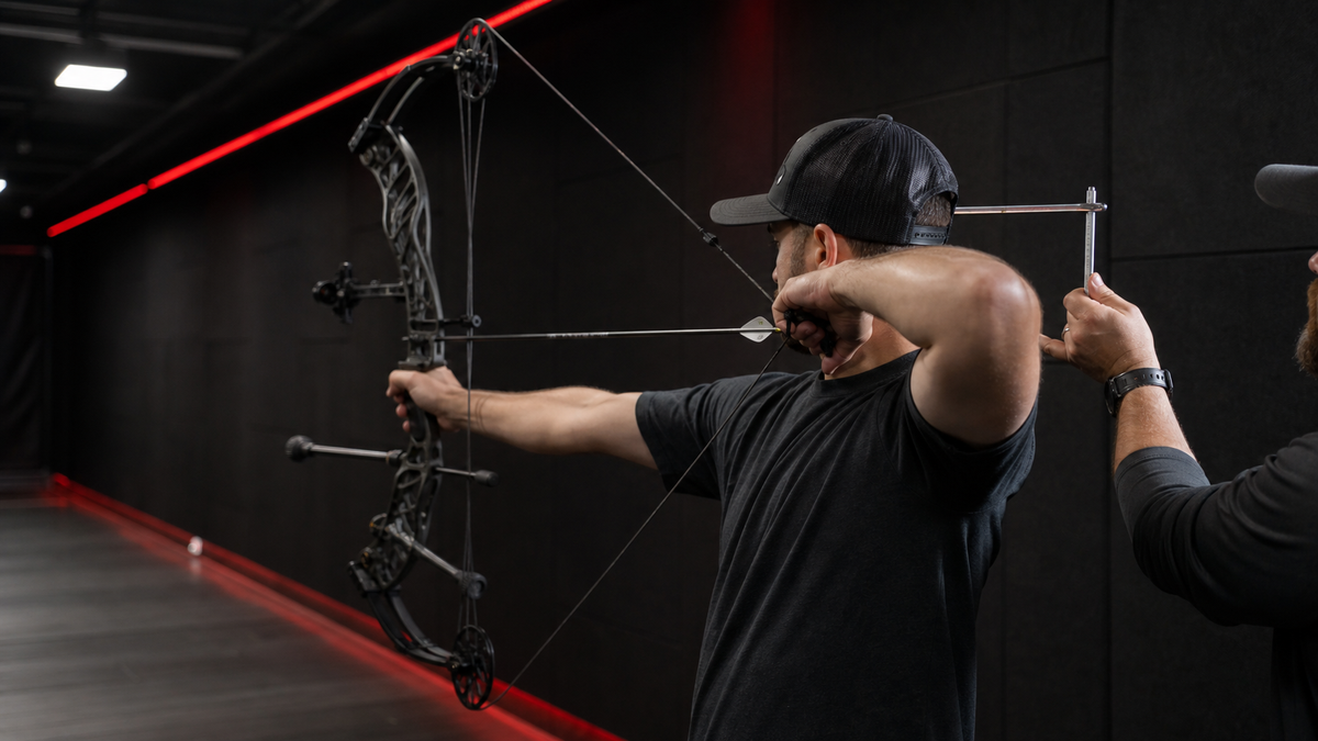 Archery technician checking an archer's draw length at full draw in an indoor range
